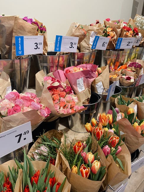 A display of various fresh flower bouquets arranged in metallic containers and wrapped in brown paper, featuring a range of colourful blooms including pink roses, orange and yellow tulips, and mixed c