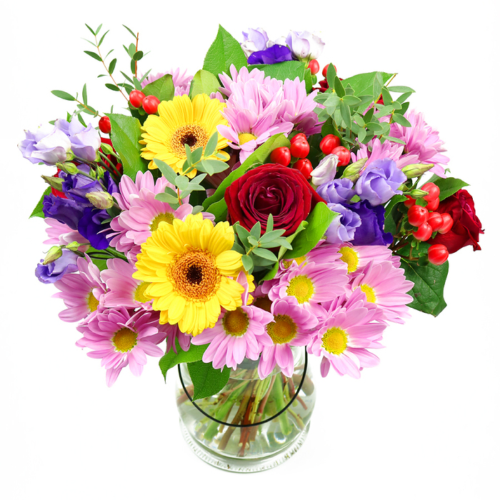 A lush, overflowing bouquet is displayed in a simple clear glass vase, photographed against a clean white background so that every colour and petal from this Gipsy Hill arrangement stands out in vivid detail. At the centre, rich crimson roses open in layered spirals, their velvety texture suggesting timeless affection and a touch of classic romance. Just offset to one side, bright yellow gerbera daisies with dark brown-orange centres beam with sunny optimism, their bold faces adding a playful, modern edge. Surrounding these focal flowers, masses of soft pink daisy-style chrysanthemums extend delicate, narrow petals around golden yellow eyes, building a cloud of pastel softness that makes the bouquet feel generous and embracing. Slender stems of lisianthus in shades of purple and cool lavender weave through the design, their gently curled, bell-shaped blooms bringing depth and a more contemporary, elegant note, like something you might see in a stylish Crystal Palace café or along Central Hill. Small clusters of round, glossy red hypericum berries are tucked among the flowers, offering bright punctuation marks of colour and a subtly festive feel. A variety of green foliage supports and frames the blooms: some leaves are broad and dark, giving structure, while lighter, elongated leaves and fine sprigs introduce an airy, garden-fresh quality, reminiscent of the greenery around Gipsy Hill's residential streets. The clear vase reveals a neat grid of stems and crystal-clear water, a quiet nod to professional floristry skills. Overall, the bouquet conveys joy, celebration, and warmth, perfect for marking milestones, thanking a friend, or bringing colour to a sunny bay window.