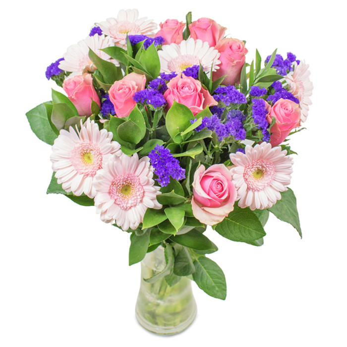 A strikingly elegant bouquet stands tall in a clear glass vase, its stems and water visible for an authentic, just-gathered effect-like a fresh cut from the edges of Norwood Park. At the centre, approximately seven to nine velvety medium pink roses, some with petals gently beginning to unfurl, create a focal point of classic romance and delicate form. They are encircled by five to seven pale pink gerbera daisies, their large, sunburst heads and soft, nearly white centres glowing under natural Gipsy Hill light. Vivid purple statice, reminiscent of wildflowers found on local walks, are carefully interspersed among the main blooms, offering lively texture and an unexpected pop of colour. Deep green foliage fans outward, lending the bouquet a lush, abundant look and a clean, woodland scent evocative of the area's green spaces. This visually stunning arrangement-crafted by florists attuned to Gipsy Hill's unique blend of urban energy and pastoral calm-is suitable for birthdays, anniversaries, Mother's Day, or as a stylish accent in homes overlooking Central Hill. The artistry and care in this hand-tied bouquet convey genuine affection, bestowing a joyful, celebratory mood upon any recipient.